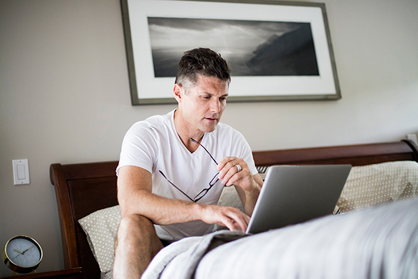 Hombre sentado en la cama mirando un ordenador portátil